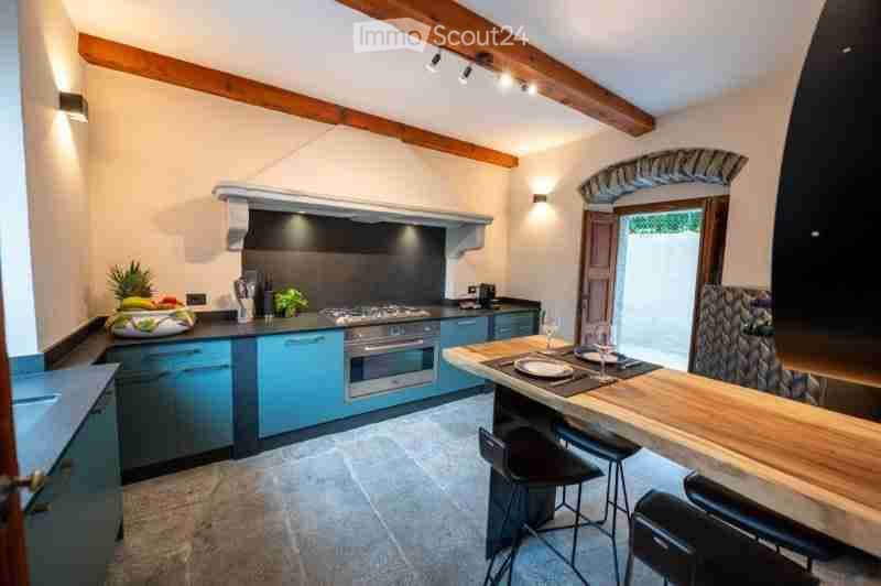 Modern kitchen with blue cabinets, stainless steel appliances, wooden island, bar stools, and fruit bowl on counter.