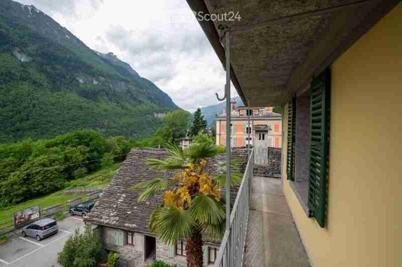 Balcony overlooking a scenic mountain view with a palm tree, a small house, and parked cars below.