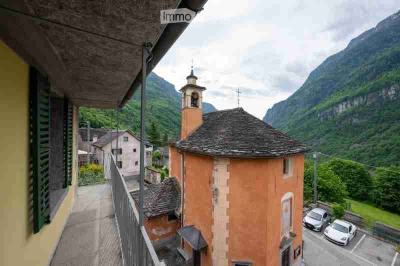 Balcony overlooking a picturesque village with a church tower, surrounded by mountains and greenery.