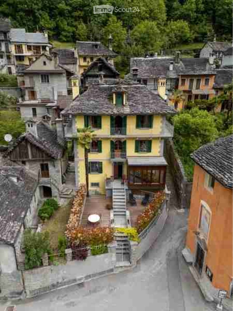Aerial view of a small village with traditional stone houses, narrow streets, and surrounding greenery.