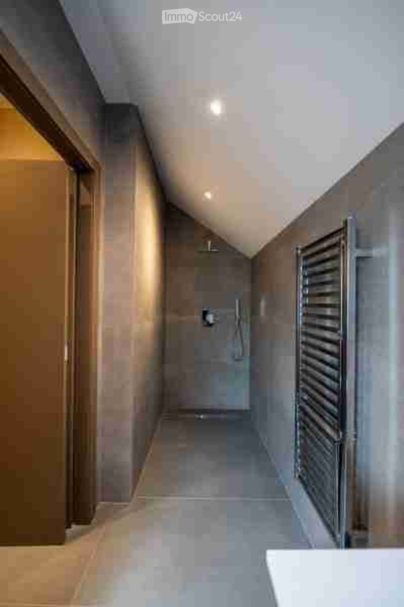 Modern hallway with sleek, contemporary design, featuring grey tiled walls and floor, recessed lighting, and a built-in towel rack on one side.
