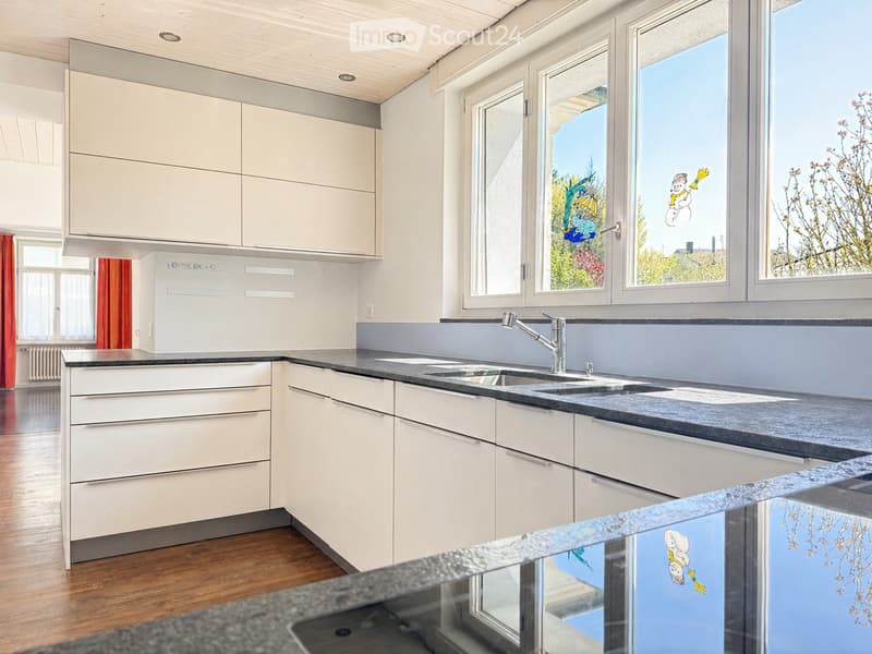 Modern kitchen with white cabinets, dark countertops, and a double sink under large windows.