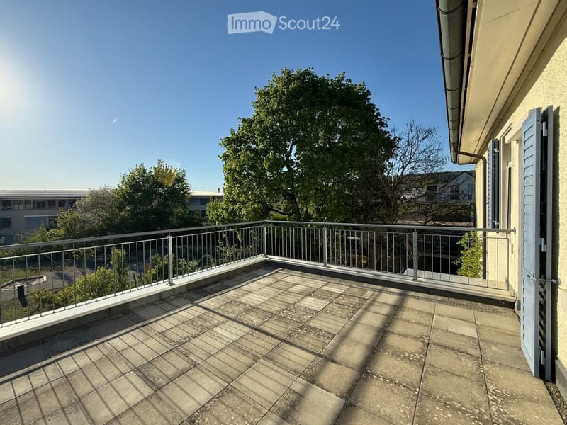 Balcony with tiled floor, metal railing, and view of trees and buildings.