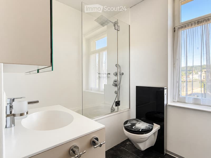 Modern bathroom with a white sink, chrome faucet, large mirror, glass-enclosed shower, and a toilet with a decorative black seat cover.