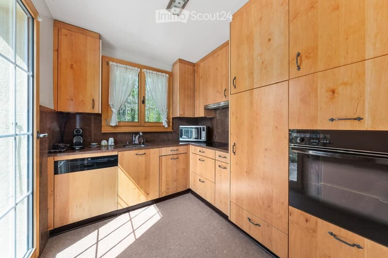 Bright kitchen with wooden cabinets, stainless steel appliances, and a large window with white curtains.