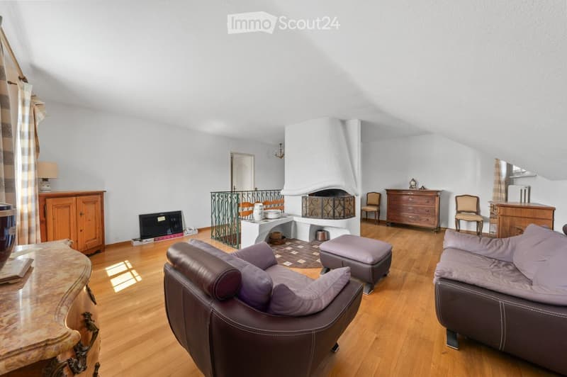 Living room with wooden flooring, fireplace, sofa, ottoman, armchair, table, cabinet, and chairs.
