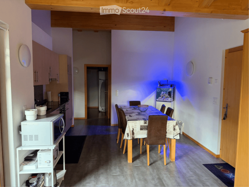 Open-plan kitchen and dining area with modern cabinets, a dining table with chairs, a fish tank, and a microwave on a shelf.
