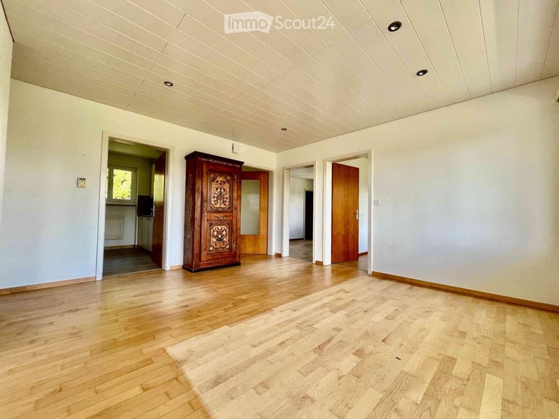 Empty room with light wooden flooring, white walls, and several doors leading to other rooms. The ceiling has recessed lighting.