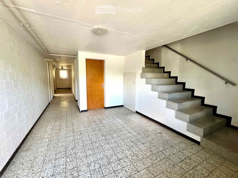 Empty hallway with tiled floor, white brick walls, a staircase with grey steps and a metal railing, and a wooden door leading to another room.