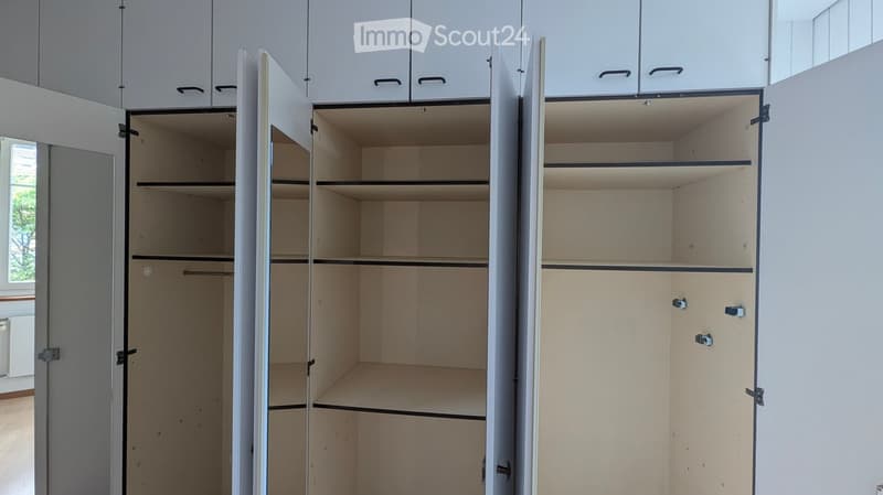 Empty built-in closet with multiple open doors, showing empty shelves and hanging space.