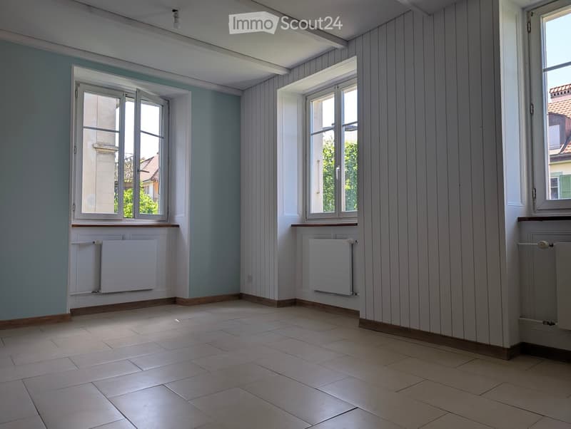 Empty room with tiled floor, light blue walls, white wooden paneling, and three windows with radiators beneath them.