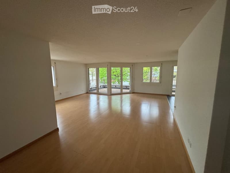 Empty room with wooden flooring, white walls, and large windows with sliding doors leading to a balcony.