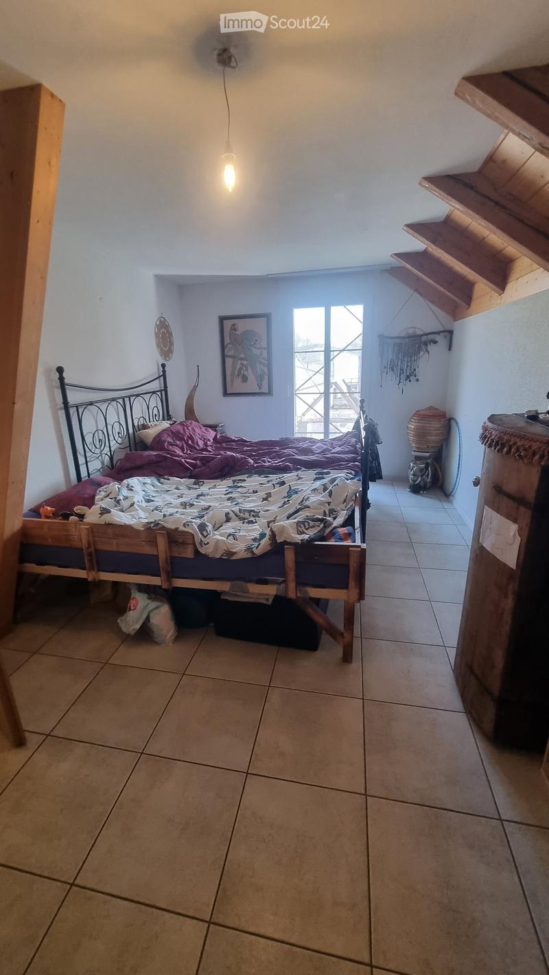 Bedroom with a wooden bed, nightstand, picture frame, shelves, and a wicker basket. The room has tiled flooring and white walls.
