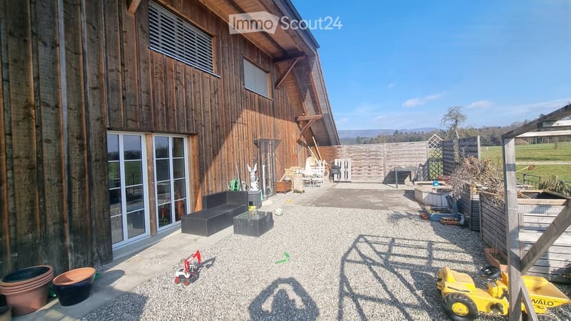 Outdoor patio area with gravel ground, wooden fence, sofa, table, and children's toys.
