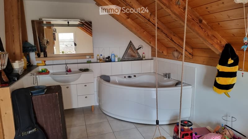 Bathroom with a white bathtub, sink, mirror, and various toiletries. Wooden slanted ceiling and tiled walls.