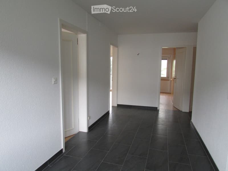 Empty hallway with dark tiled flooring and white walls, featuring several open doors leading to other rooms.