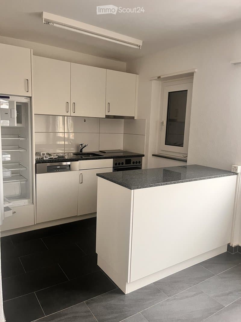 Modern kitchen with white cabinets, black countertop, stainless steel appliances, and a window above the sink.