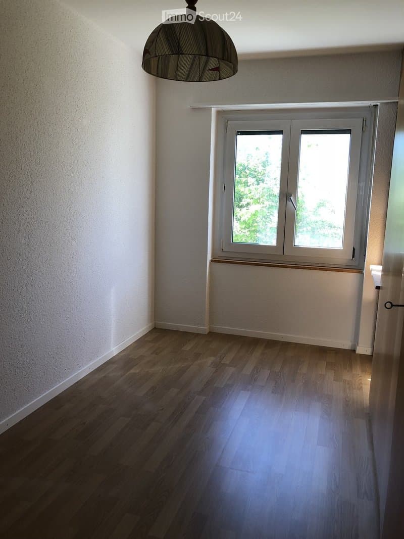 Empty room with wooden flooring, white walls, a window with double panes, and a hanging lamp.