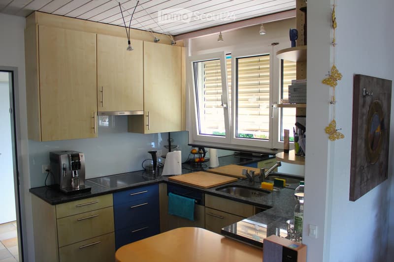 Modern kitchen with light wood cabinets, granite countertops, stainless steel appliances, and a central island with a round wooden table.
