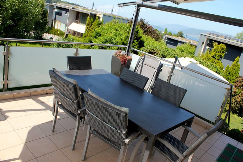 Balcony with a black table and four wicker chairs, surrounded by greenery and a scenic view of the landscape.