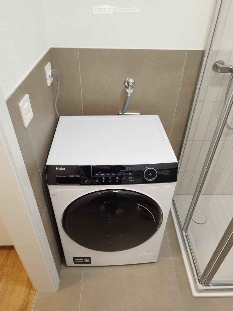 A compact bathroom with a modern white washing machine placed next to a glass shower enclosure.