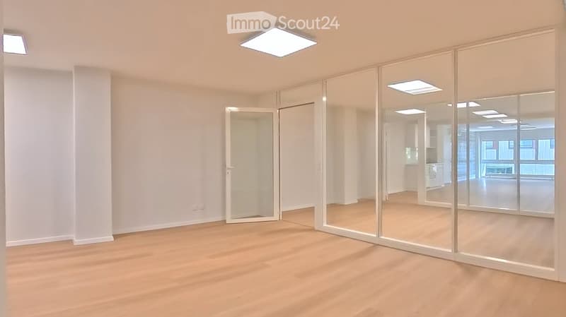 Empty room with light wooden flooring, white walls, and large glass partitions. No furniture or equipment visible.