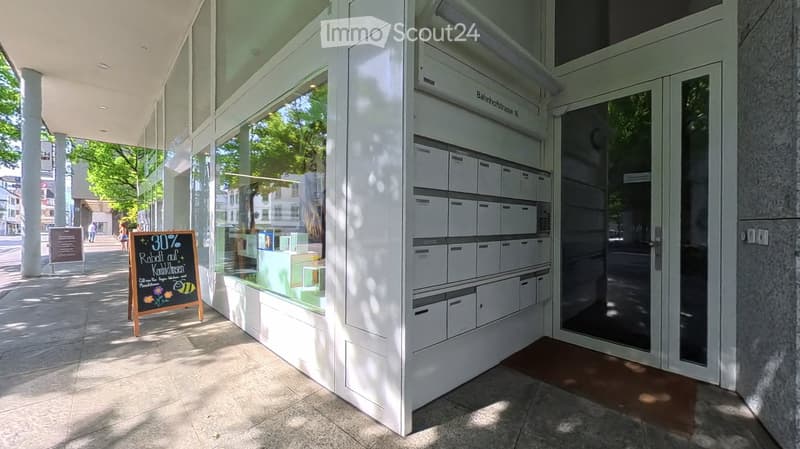 Modern building entrance with glass doors, mailboxes, and a sign advertising a 30% discount on baby clothes.
