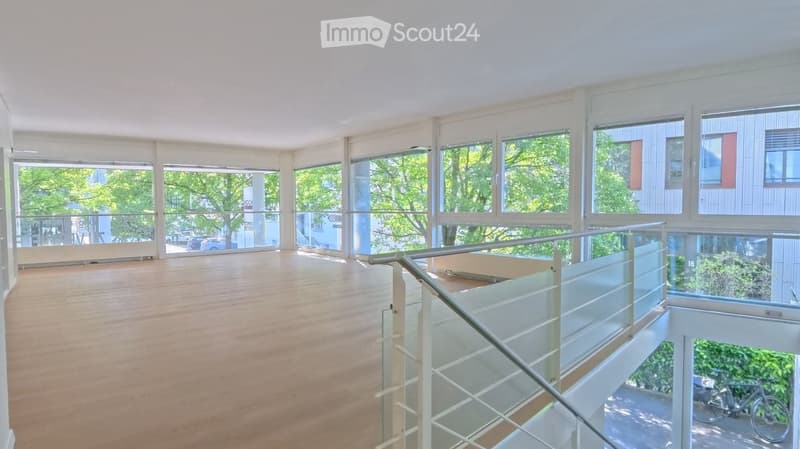 Open, empty room with wooden flooring and large windows, featuring a modern glass staircase leading to an upper level.
