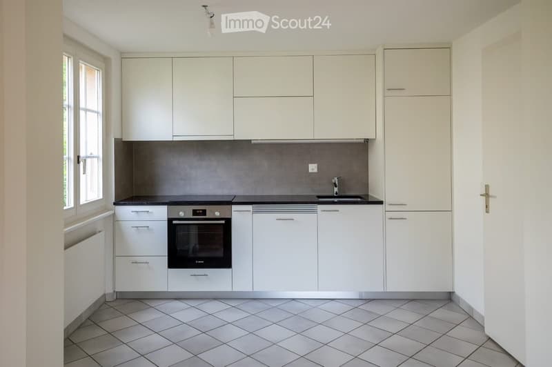 Modern kitchen with white cabinets, black countertop, and stainless steel appliances including an oven and sink.