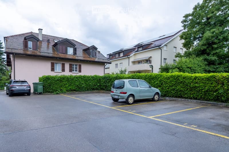 Residential area with two houses, a parking lot, and two parked cars.