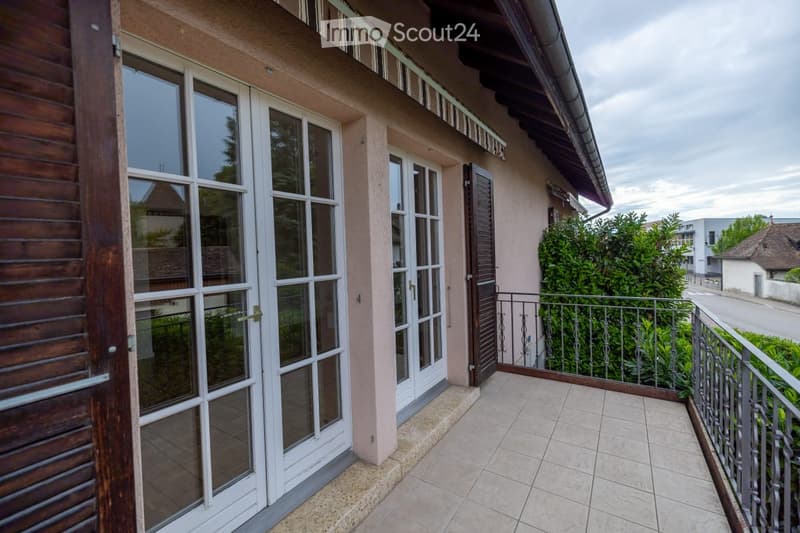 Balcony with tiled floor, metal railing, and large windows leading to the interior of the house.