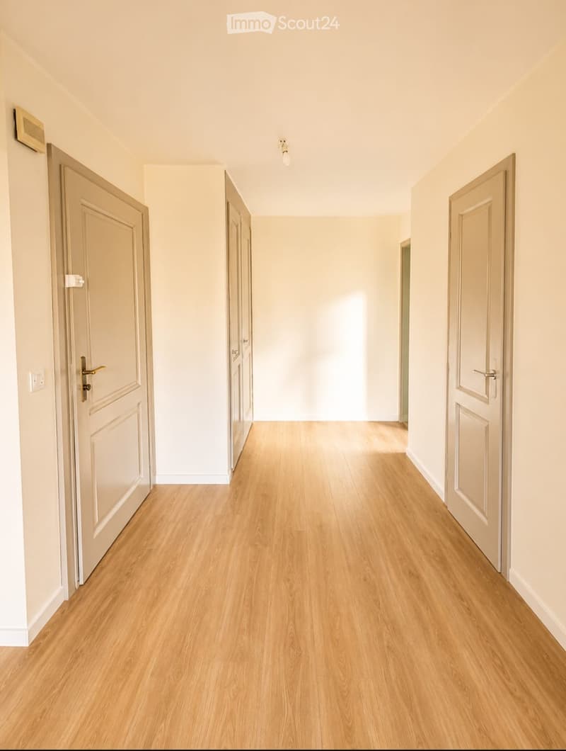 Empty hallway with light wooden flooring, white walls, and several closed doors on both sides.