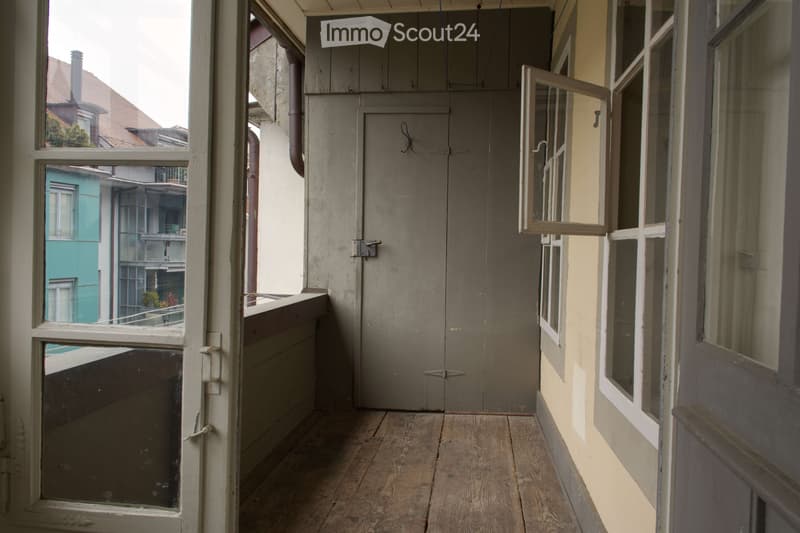 Balcony with wooden floor, glass doors, and windows, leading to a room with a door and windows