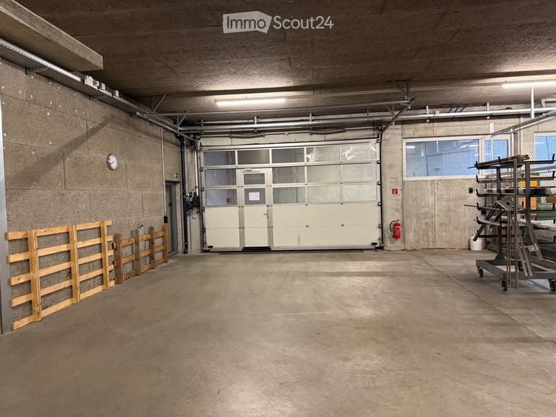 Empty garage with concrete walls and floor, large garage door, and minimal storage items.