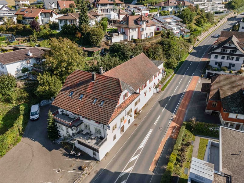 Aerial view of a residential area with multiple houses, red-tiled roofs, and surrounding greenery.