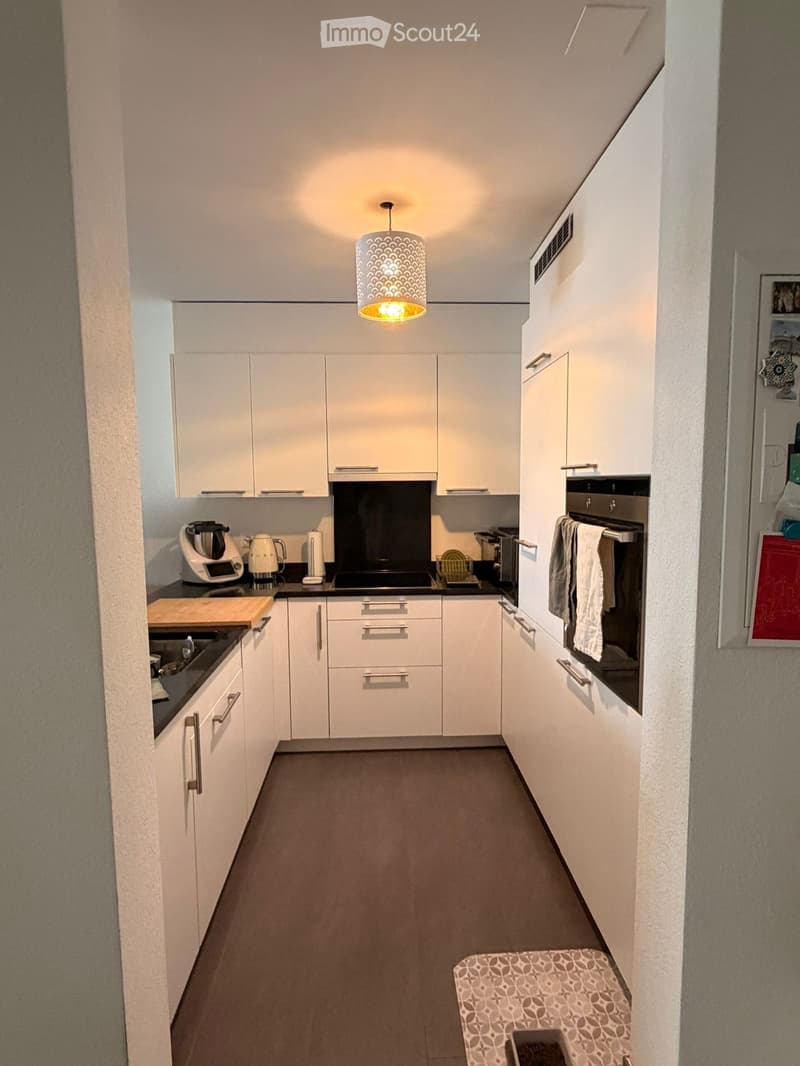 Modern kitchen with white cabinets, stainless steel appliances, and a central island. Features include a built-in oven, a sink with a faucet, and various kitchen appliances on the counter.