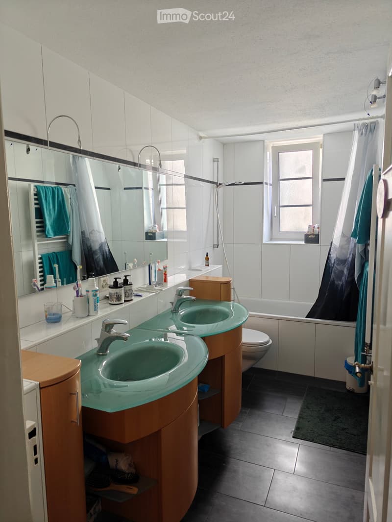 Modern bathroom with double sink, mirror, toothbrush holders, toothpaste, and a bathtub with a shower curtain.