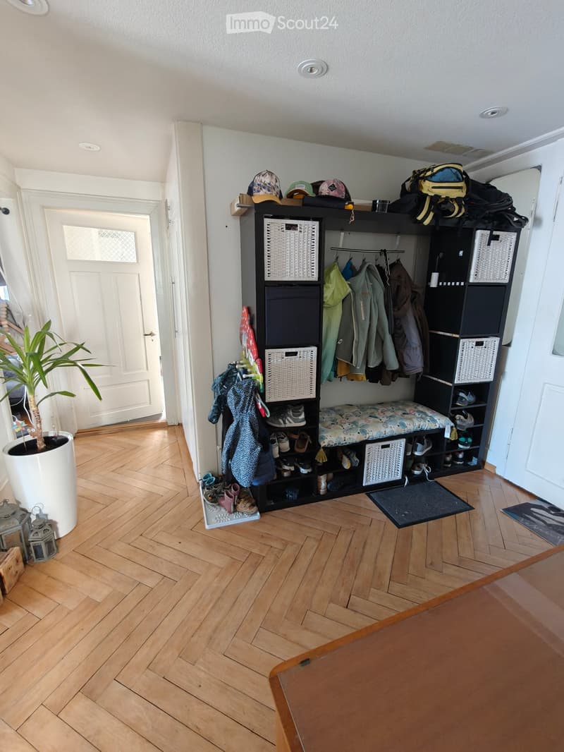 Hallway with wooden flooring, coat rack, shoe storage, and a small bench. Features a potted plant and decorative lanterns on the left side.