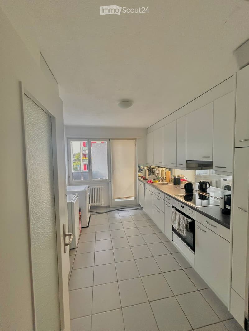 Modern kitchen with white cabinets, tiled floor, and stainless steel appliances including a refrigerator, oven, stove, and sink. A window provides natural light, and a radiator is visible near the window.