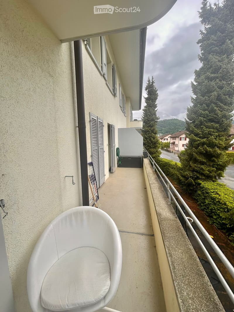 Balcony with a white chair, railing, and view of trees and houses.