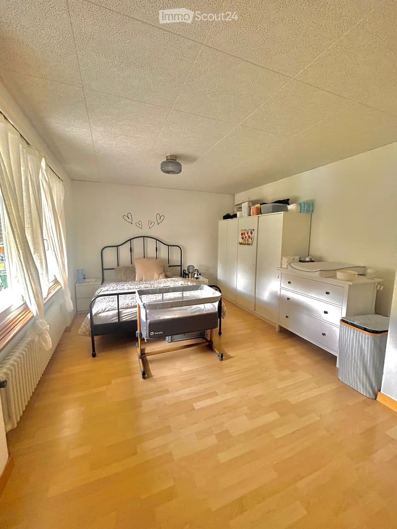 Bright bedroom with wooden flooring, a metal-framed bed, a baby crib, a wardrobe, a dresser, and a nightstand.