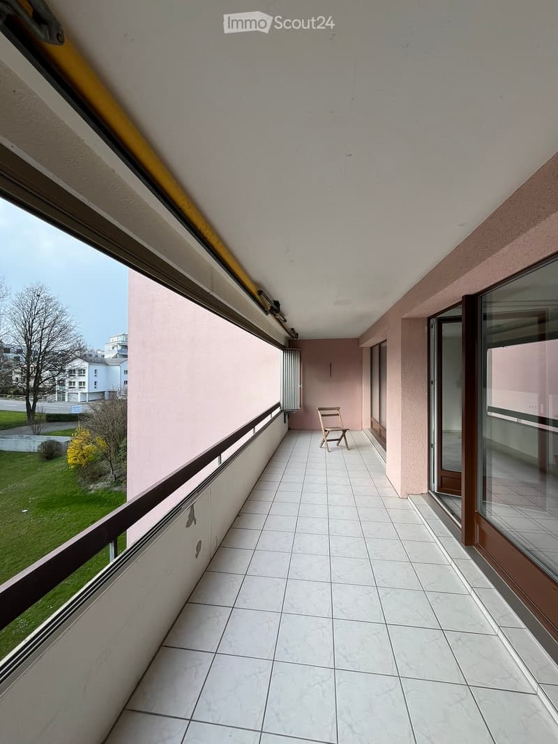 Balcony with tiled floor, white walls, and a single wooden chair placed near the entrance.