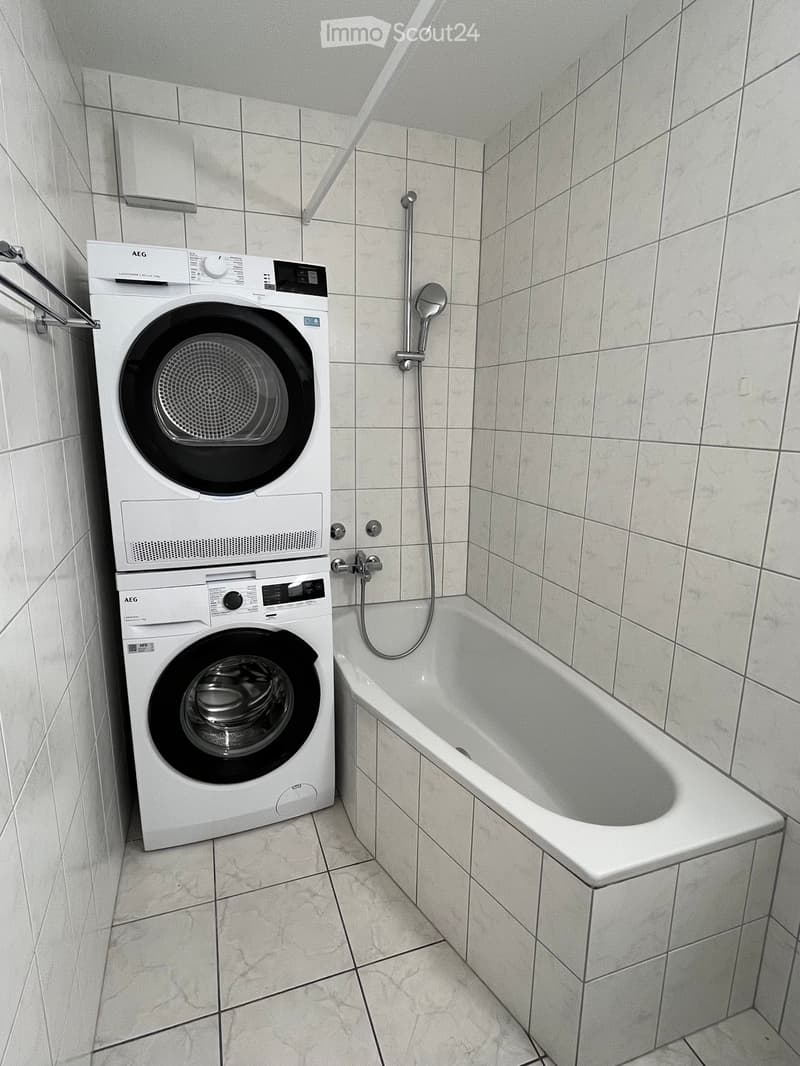 Bathroom with a bathtub and a stacked washing machine and dryer unit.