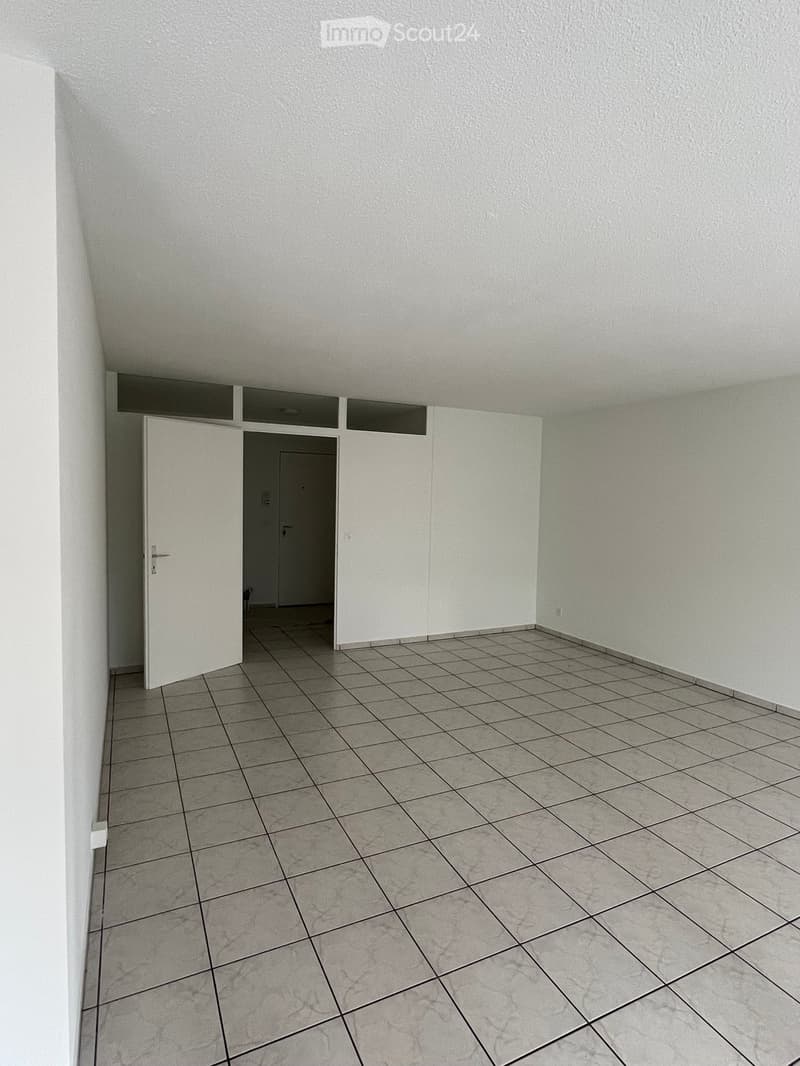 Empty room with tiled floor and white walls, featuring an open doorway leading to another space.
