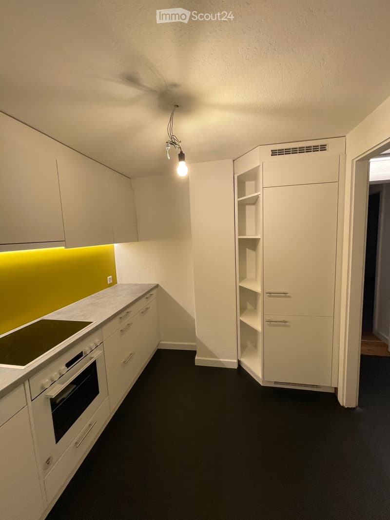 Modern kitchen with white cabinets, a built-in oven, and a sleek countertop. Features include a bright yellow backsplash and a hanging light fixture.