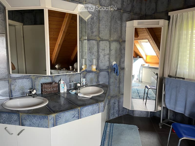Bathroom with two sinks, mirrors, cabinets, and a towel rack. The room features blue tiled walls and a slanted wooden ceiling.