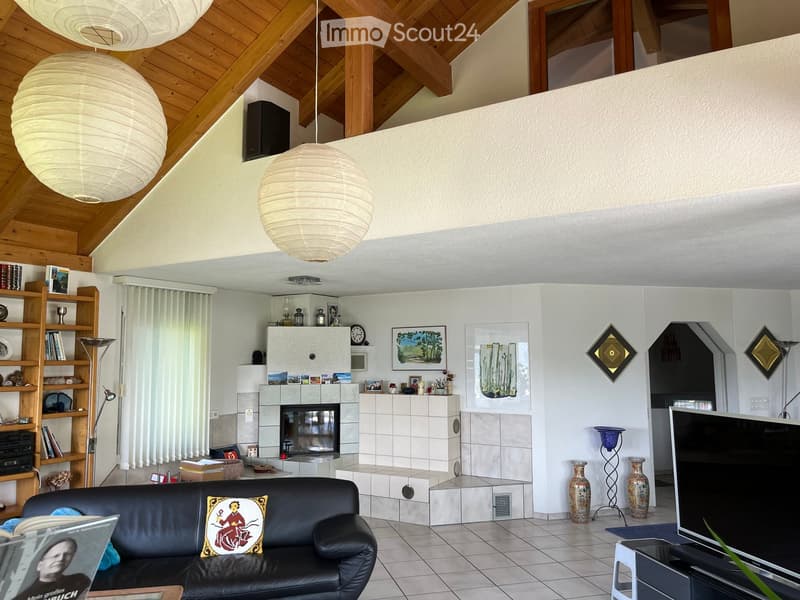 Living room with a black leather sofa, fireplace, bookshelf, decorative vases, and a television. The room features a wooden ceiling with exposed beams and large paper lanterns as lighting.