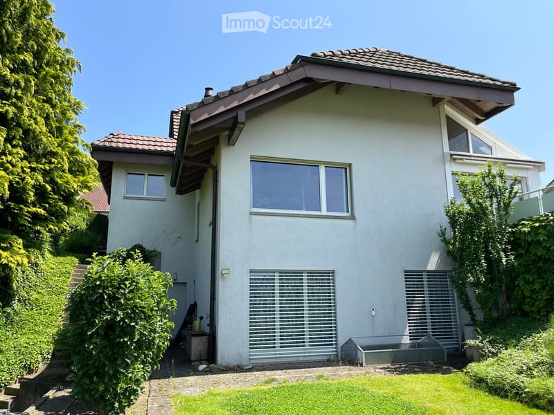 Two-story white house with a tiled roof, large windows, and a well-maintained garden with green grass and shrubs.
