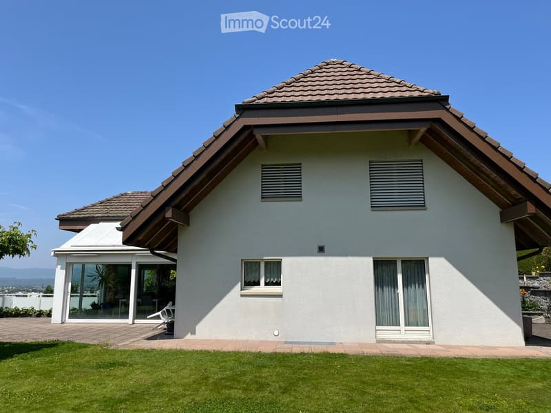 Single-story house with a tiled roof, white exterior walls, large windows, and a covered patio area with outdoor furniture.