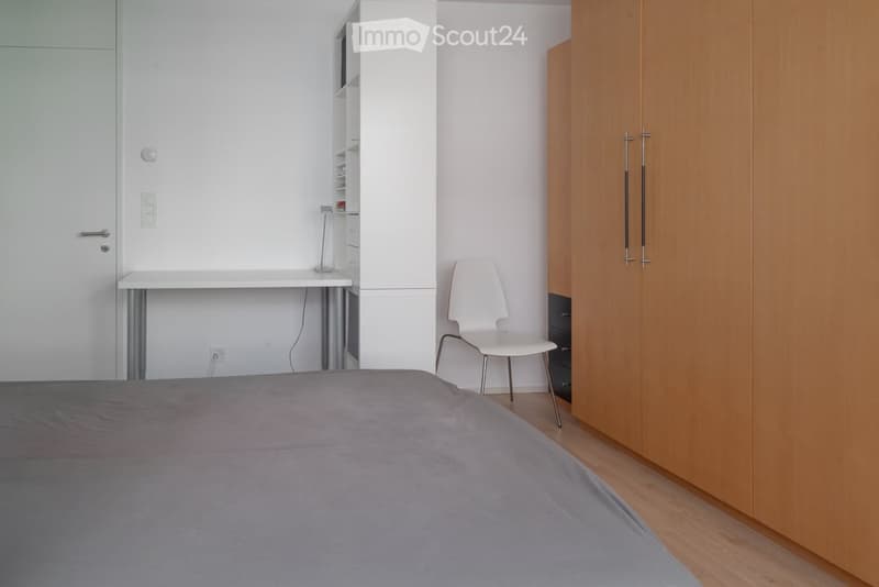 Modern bedroom with a grey bed, white chair, desk, and built-in wardrobe with mirrored doors.